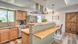 A modern kitchen with wooden cabinets, a tiled backsplash, stainless steel appliances, and pendant lighting.