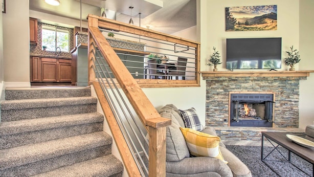 A staircase with wooden railings, a stone fireplace, a flat-screen TV above the fireplace, and a dining area with a table and chairs.