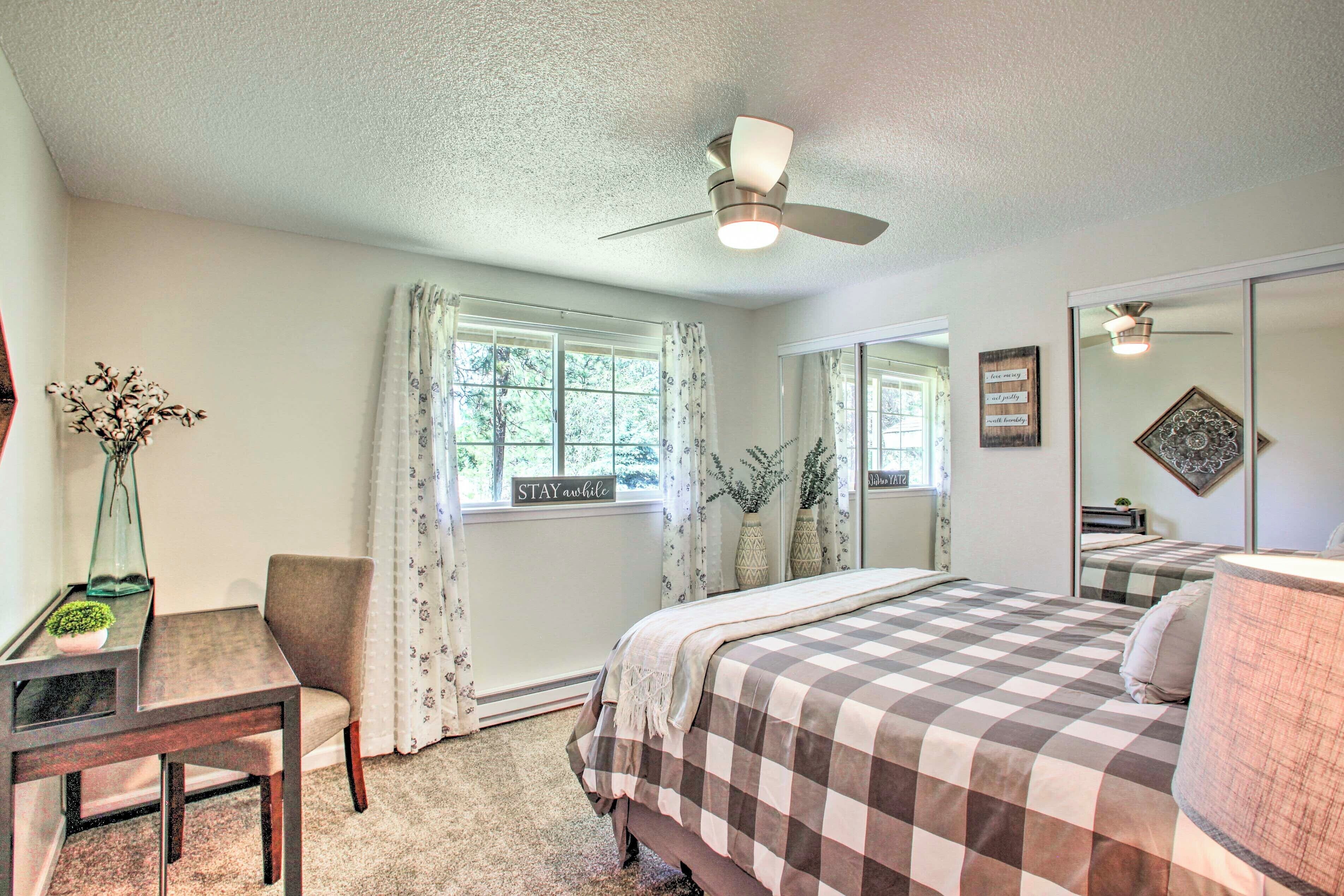 A bedroom with a bed, a desk, a chair, a ceiling fan, and a window with curtains.