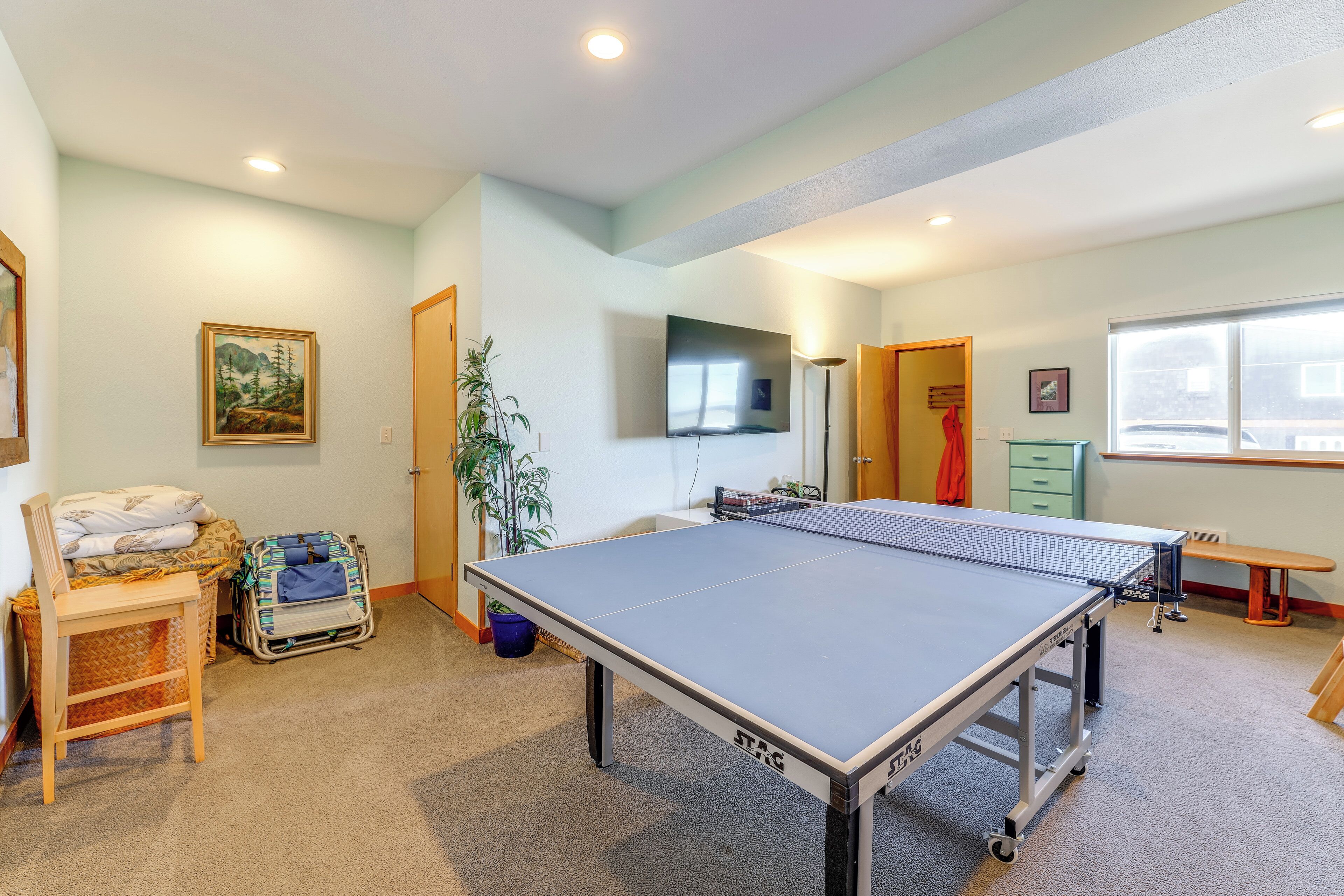 A room with a ping pong table, a bed, a chair, a suitcase, and a television on the wall.