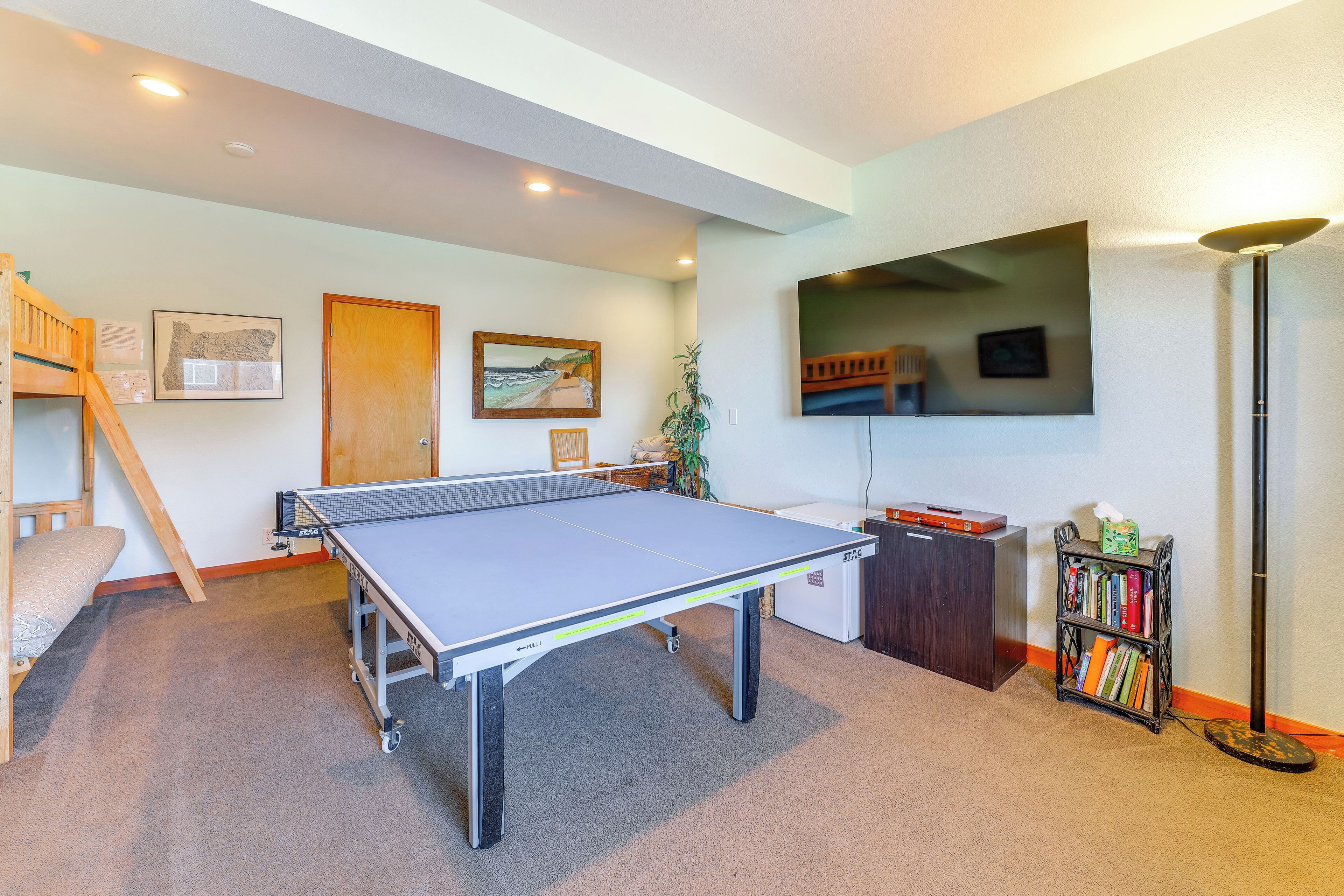 A room with a ping pong table, a bookshelf, a desk, a plant, and a wooden ladder.