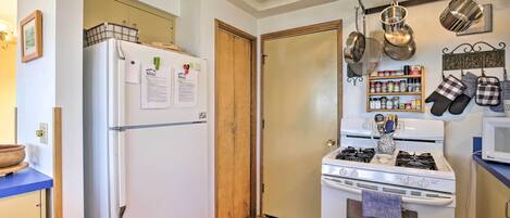 A compact kitchen with a refrigerator, stove, and microwave. There are hanging pots and a spice rack.