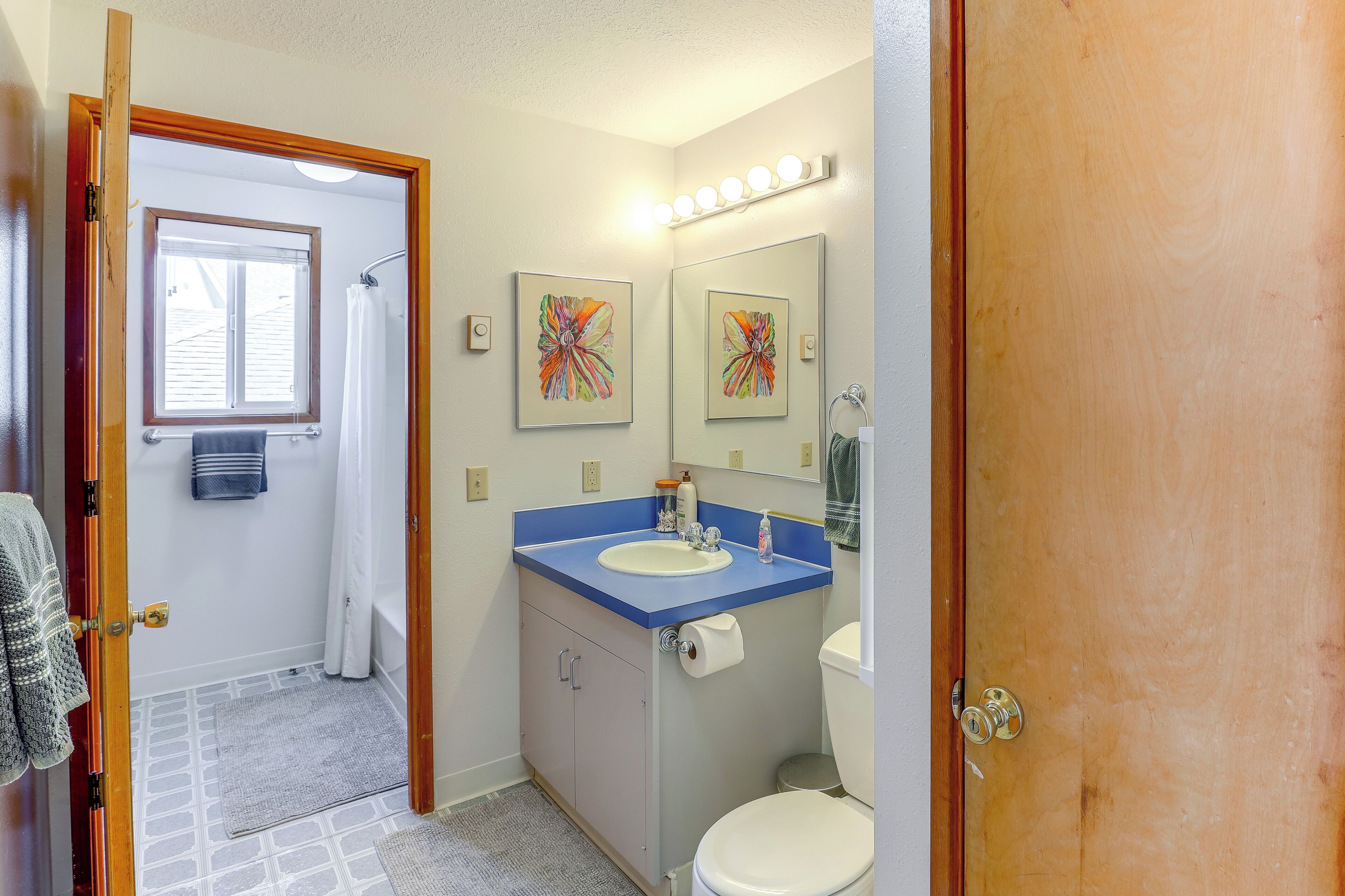 A bathroom with a blue countertop sink, a white toilet, and a shower with a window above.