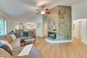 A spacious living room with a stone fireplace, a ceiling fan, and a view into the kitchen. - Family Retreat Near Beach on Lake Charlevoix (Charlevoix)