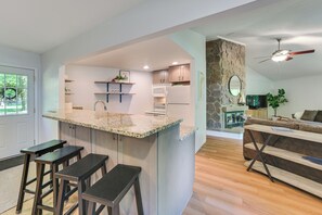 Una cocina moderna con una isla central, taburetes de bar, una pared de acento de piedra y una zona de estar acogedora con sofá y mesa de centro.