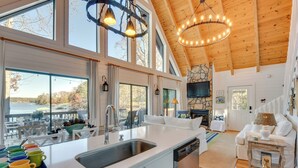 A spacious kitchen with a large island, a dining area with white furniture, and a living room with a fireplace. - Beautiful Lake Keowee Home w/ Boat Dock & Fire Pit (Seneca)