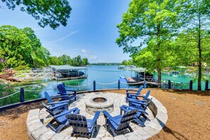 A lakeside patio with Adirondack chairs, a fire pit, and a dock extending into the water. - Beautiful Lake Keowee Home w/ Boat Dock & Fire Pit (Seneca)