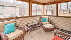 Une véranda couverte, aménagée avec des meubles en osier, notamment deux fauteuils et une petite table.