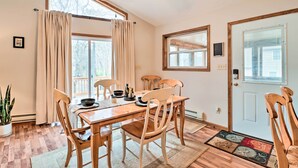 Une salle à manger avec une table et des chaises en bois, un ventilateur de plafond et de grandes fenêtres avec des rideaux.