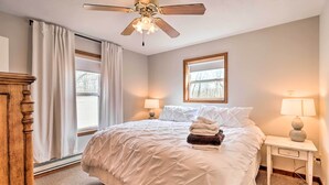 Une chambre à coucher avec un lit, deux lampes de chevet, un ventilateur de plafond et une fenêtre avec des rideaux.