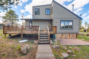 A two-story house with a wooden deck, stone foundation, and a stone chimney. - Cozy Red Feather Lakes Retreat w/ Deck & Yard (Red Feather Lakes)