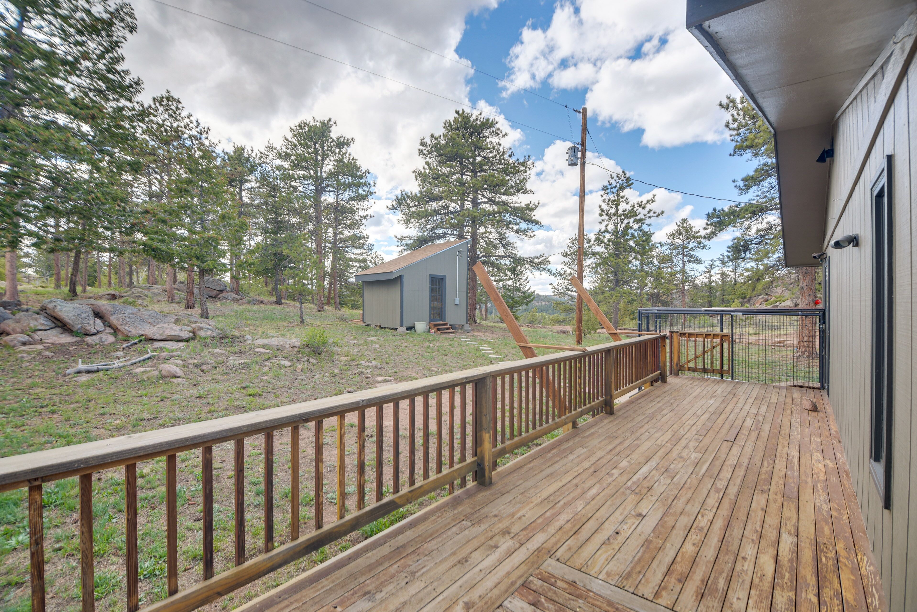 A wooden deck with a railing, a small shed, and a fenced yard with trees and rocks.
