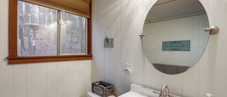 A bathroom with a large mirror, a toilet, a sink with a faucet, and a window with blinds.