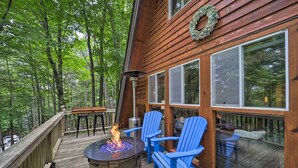 A wooden deck with a stone fire pit and blue Adirondack chairs, surrounded by a forest. - Private Hot Tub: Cabin 1 Mi to Beech Mountain! (Banner Elk)