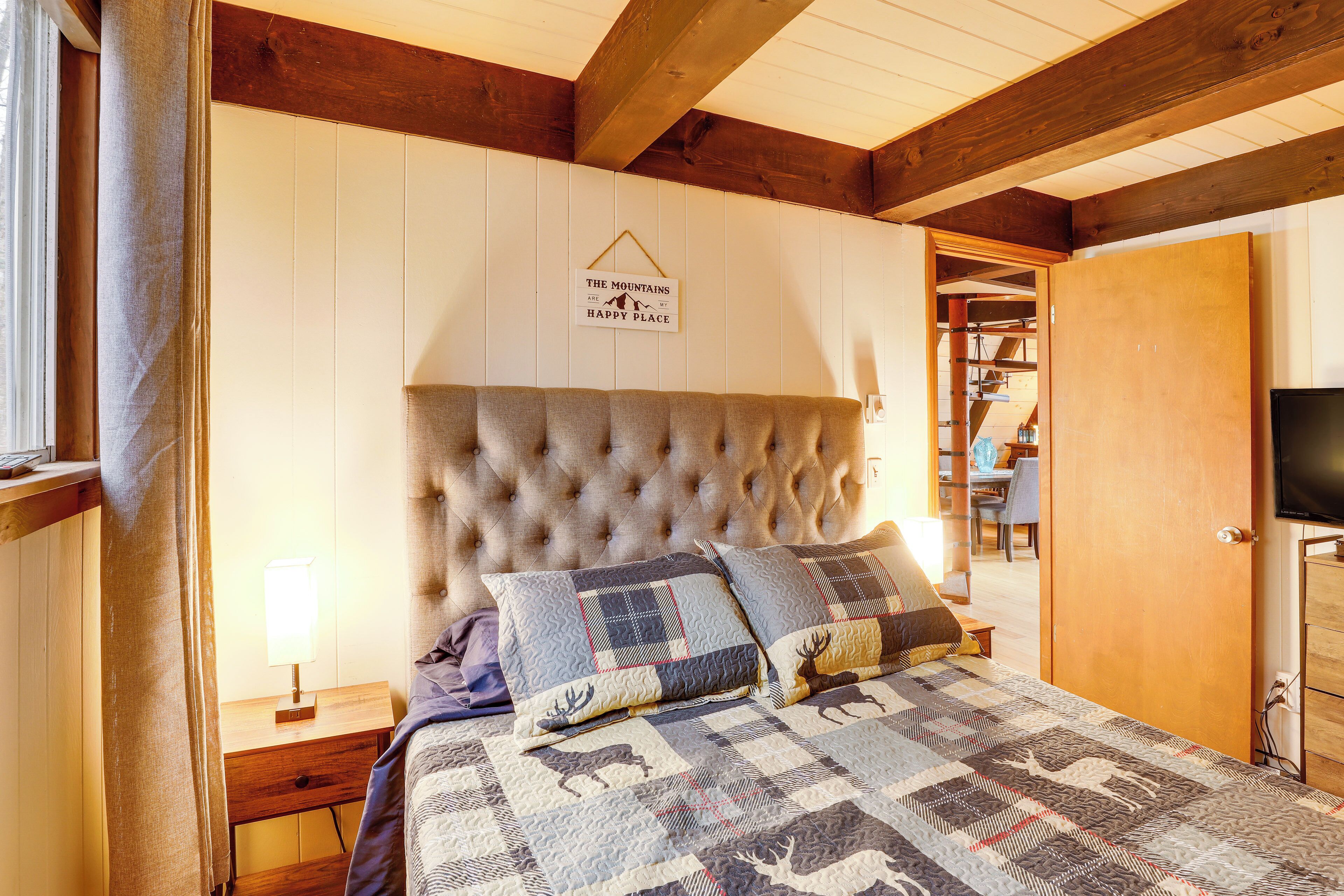 A bedroom with a tufted headboard, a quilt with animal prints, a bedside lamp, and a sign on the wall.