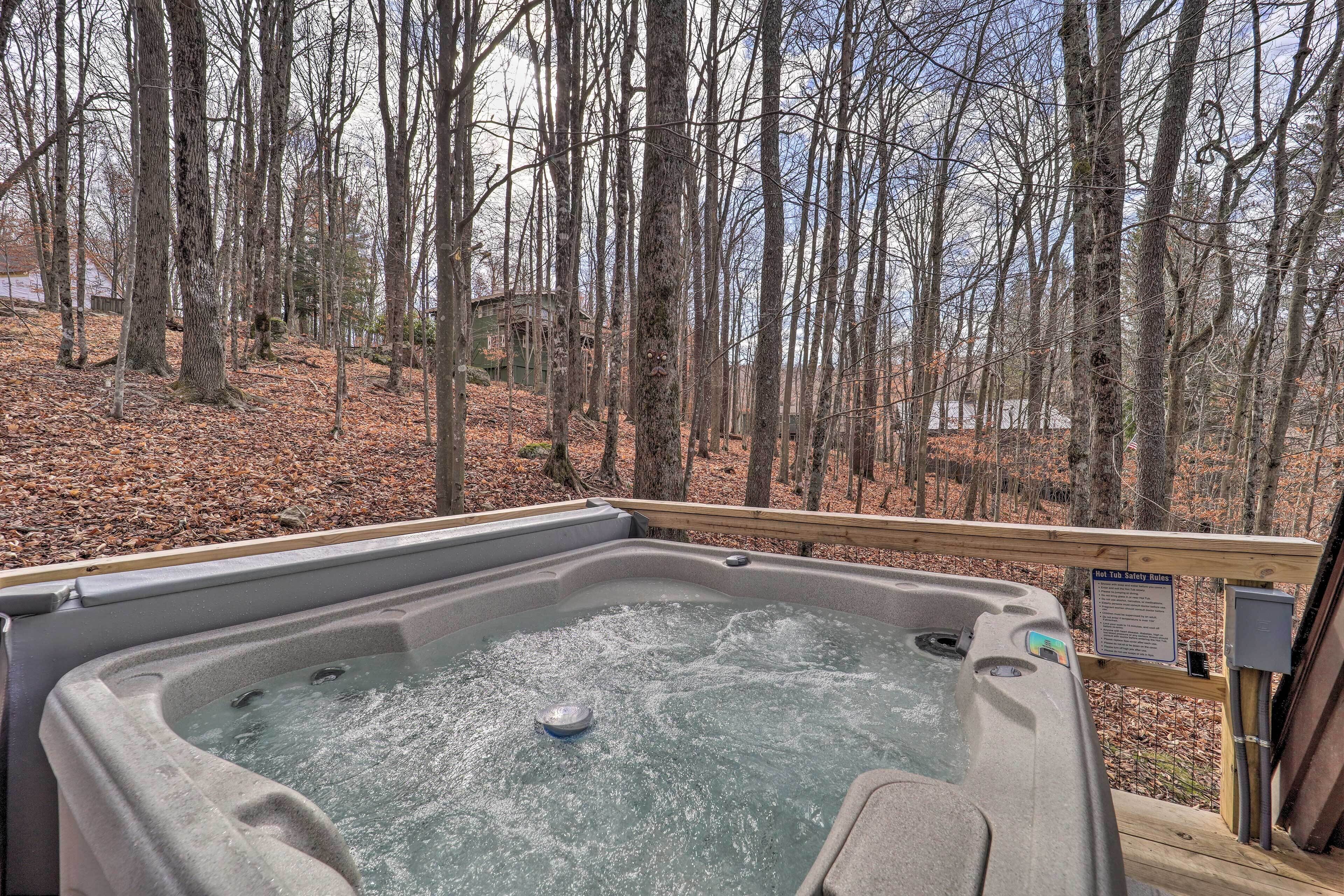 Un jacuzzi rodeado por una terraza de madera, con un área boscosa al fondo.