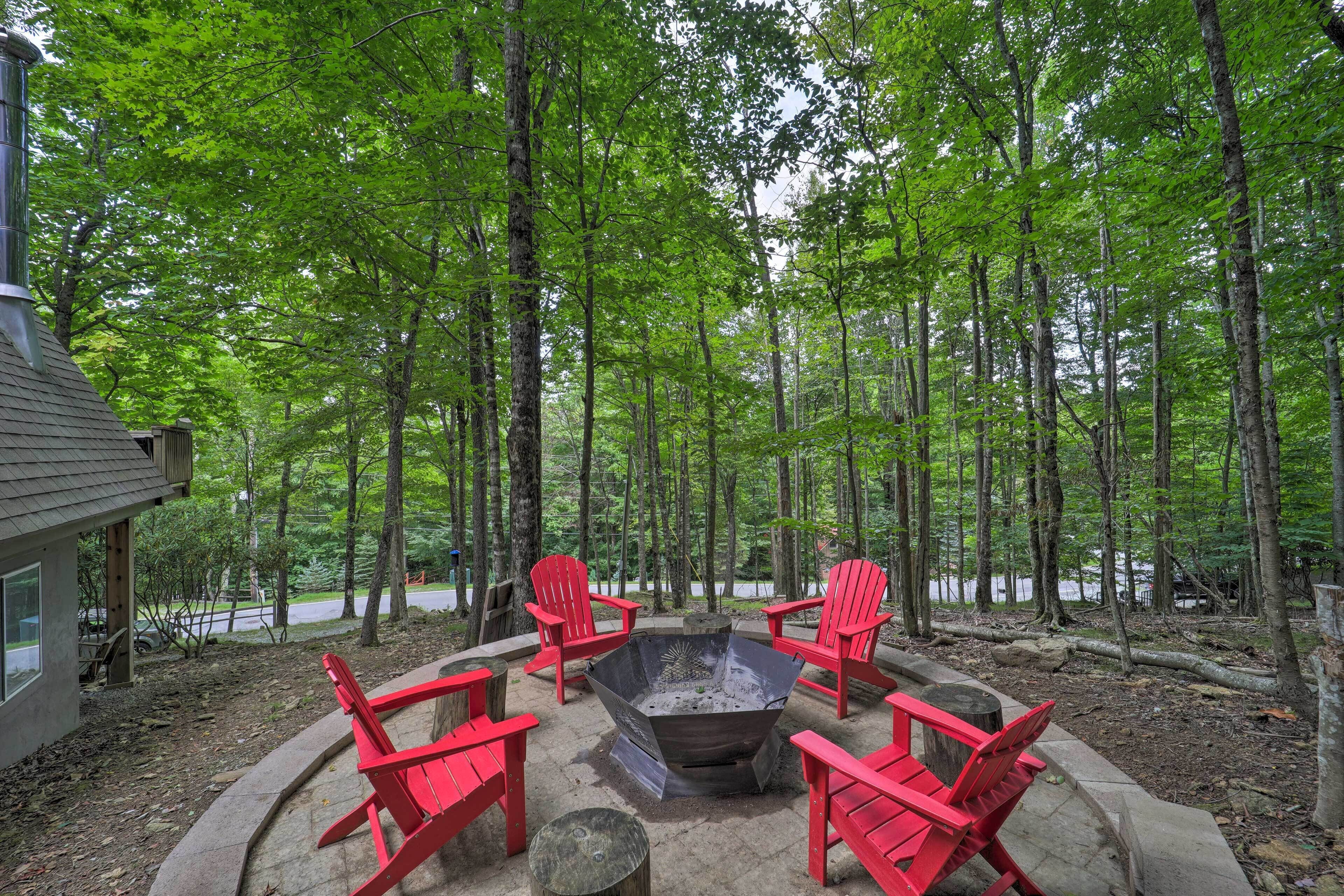 A forested area with a fire pit and red chairs.