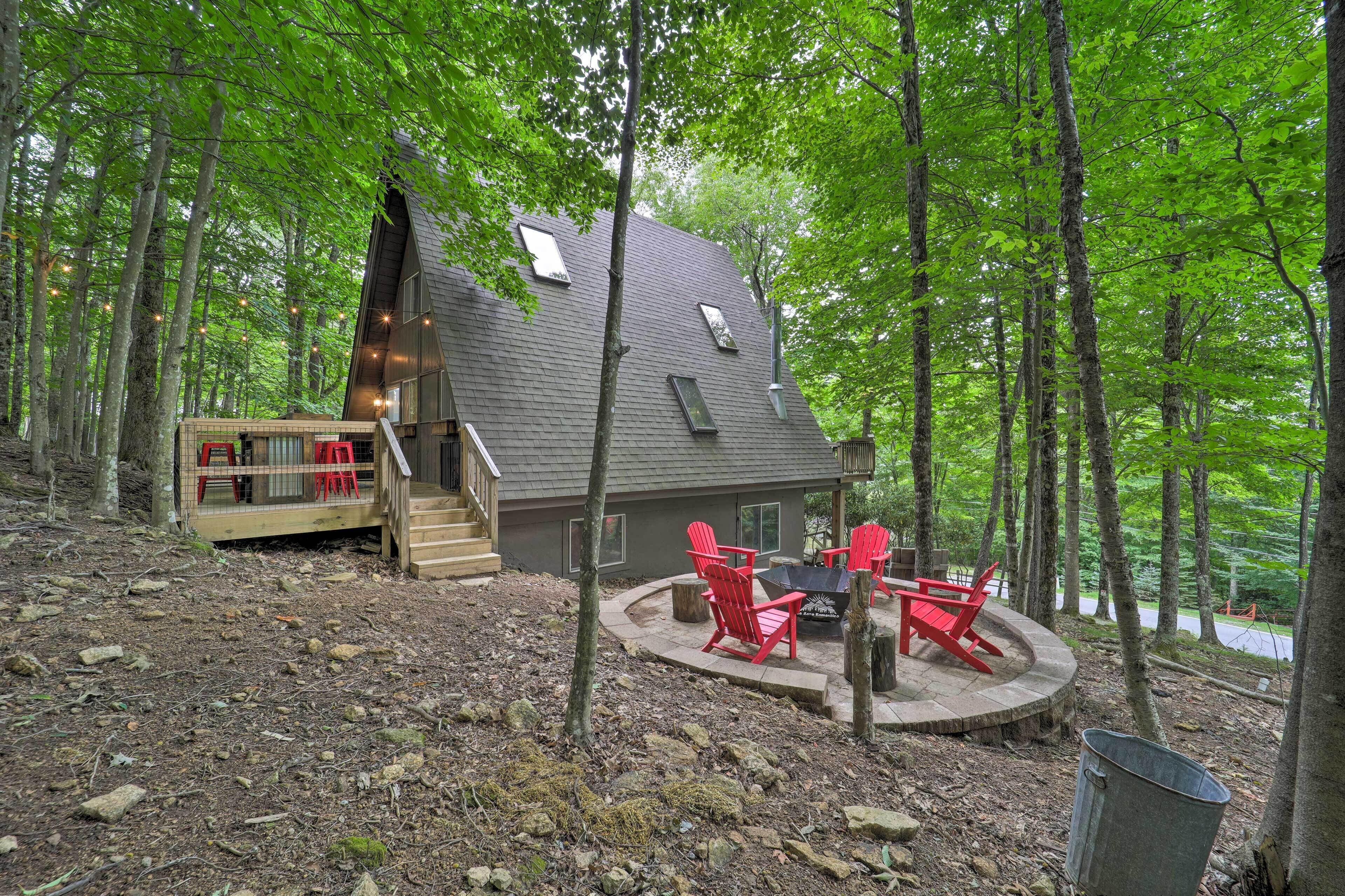 A cabin with a deck, red Adirondack chairs, and a stone fire pit.