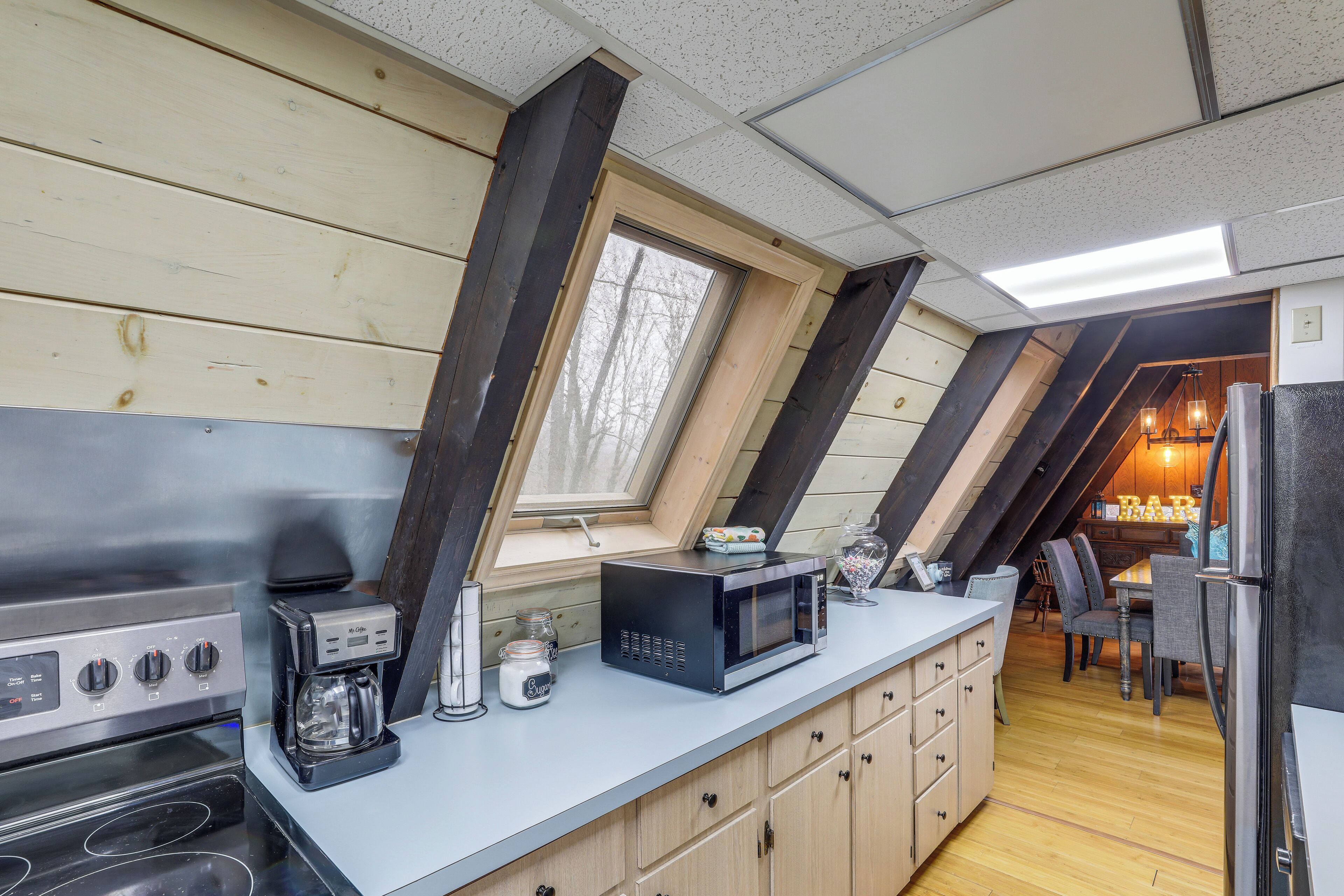 Eine Küche mit Einbauherd, Mikrowelle und Kaffeemaschine. Ein Fenster bietet Blick ins Freie, und ein Essbereich mit Tisch und Stühlen lädt zum Verweilen ein.