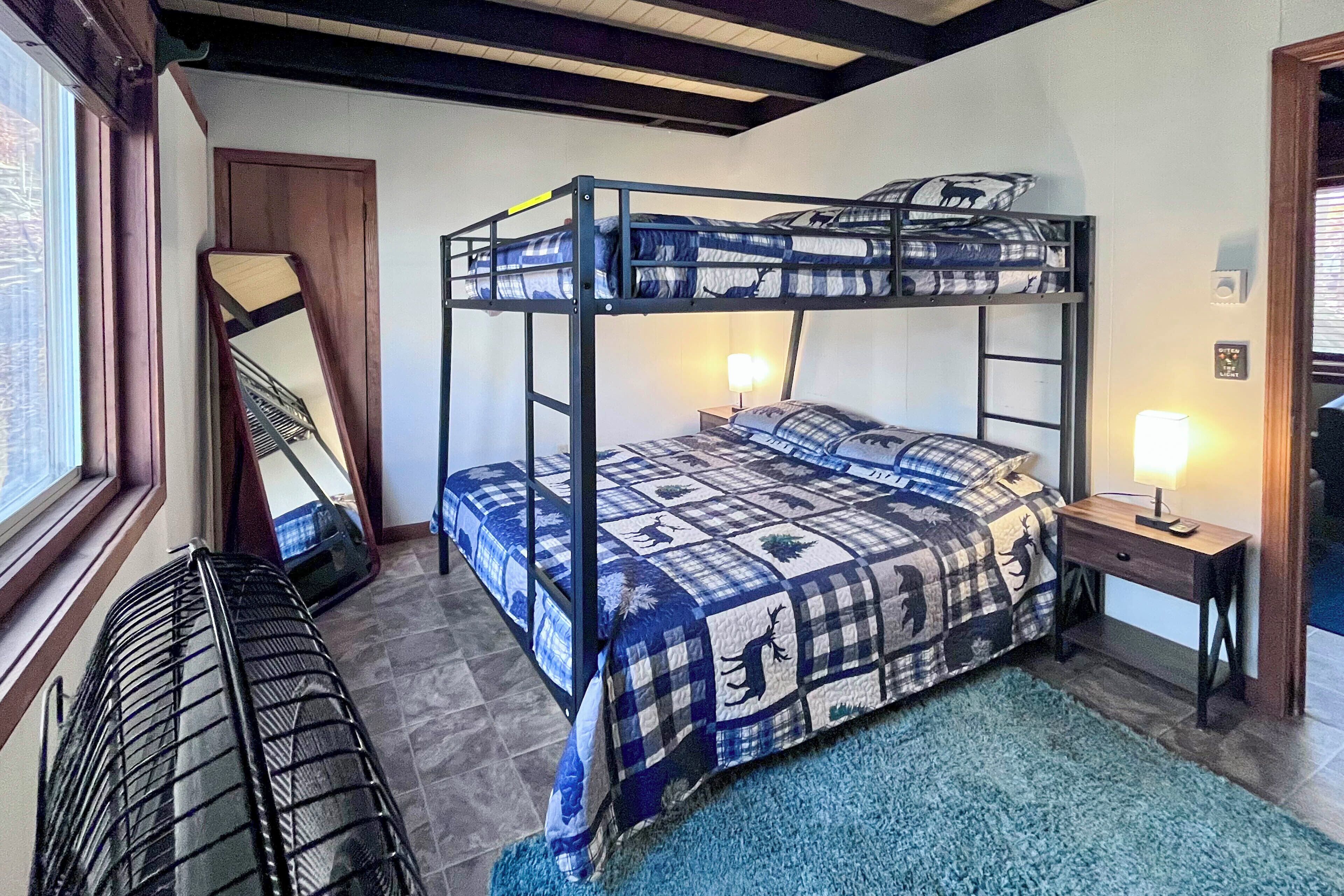 A bunk bed with a checkered blanket, a bedside table with a lamp, and a window with blinds.