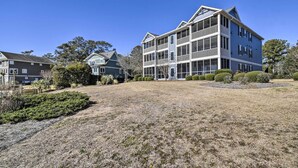 A multi-story residential building with a prominent balcony on the second floor, surrounded by a well-maintained lawn and mature trees.