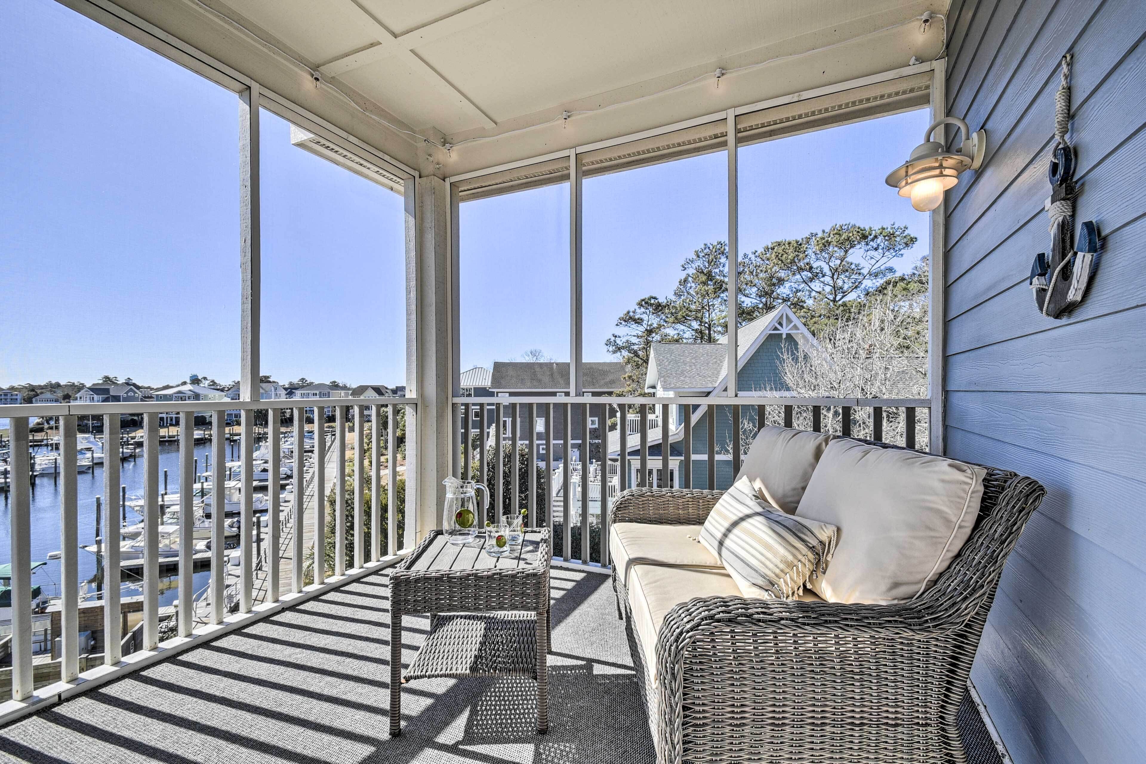 A balcony with wicker furniture, a table with a pitcher, and a view of a marina.