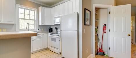 A kitchen with white cabinets, a refrigerator, an oven, and a window.