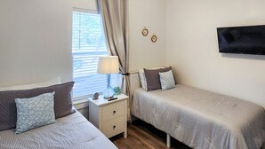 Ein Schlafzimmer mit zwei Betten, einem Nachttisch, einer Lampe und einem Fernseher an der Wand.