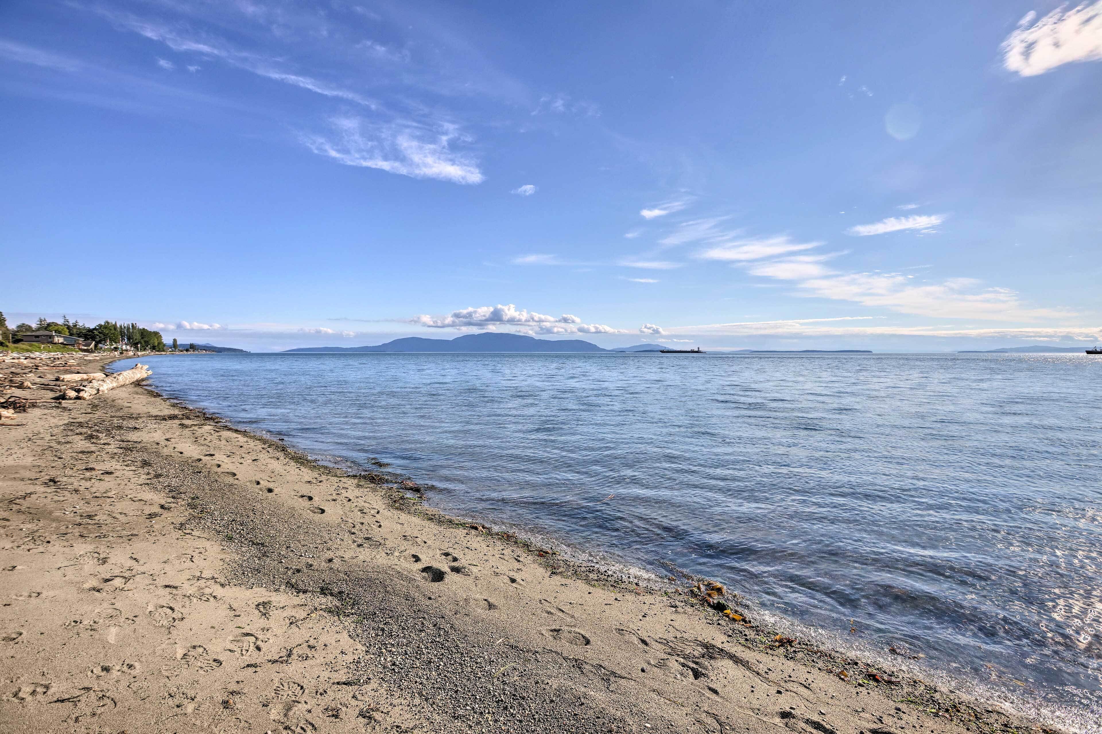 A beach with clear skies, calm water, and distant mountains.