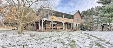 A two-story wooden house with a porch, surrounded by snow-covered ground and trees.