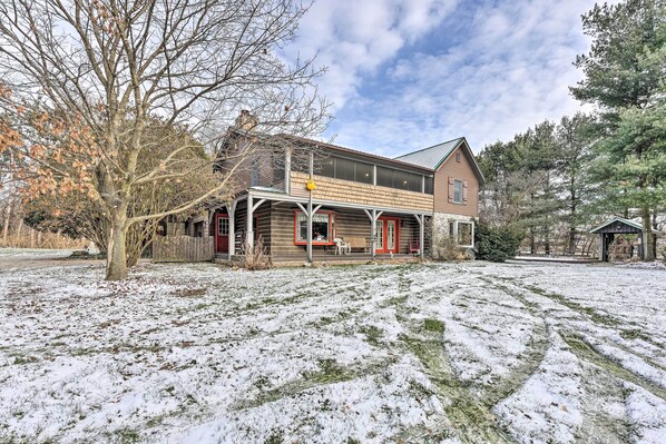 A two-story wooden house with a porch, surrounded by snow-covered ground and trees. - Primitive Goshen Pine Lodge With Fireplace! (Middlebury)