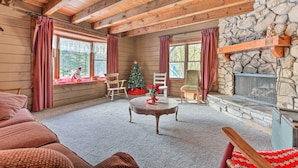 A cozy cabin interior with a stone fireplace, wooden beams, and a Christmas tree. - Primitive Goshen Pine Lodge With Fireplace! (Middlebury)