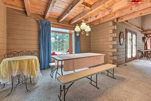 A rustic wooden cabin interior with a dining table, bench, and a large window with a view of trees. - Primitive Goshen Pine Lodge With Fireplace! (Middlebury)