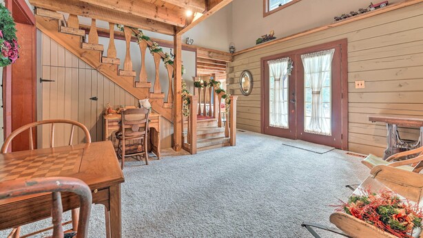A wooden staircase with a wooden railing, a dining table with chairs, a small table with a lamp, and a bench with a wreath. - Primitive Goshen Pine Lodge With Fireplace! (Middlebury)