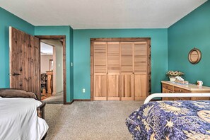 A bedroom with teal walls, a wooden wardrobe, a bed with a patterned bedspread, and a bedside table with a vase and a cup. - Primitive Goshen Pine Lodge With Fireplace! (Middlebury)