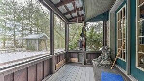 A covered porch with a view of a snowy landscape, a wooden bench, and a blue mat. - Primitive Goshen Pine Lodge With Fireplace! (Middlebury)