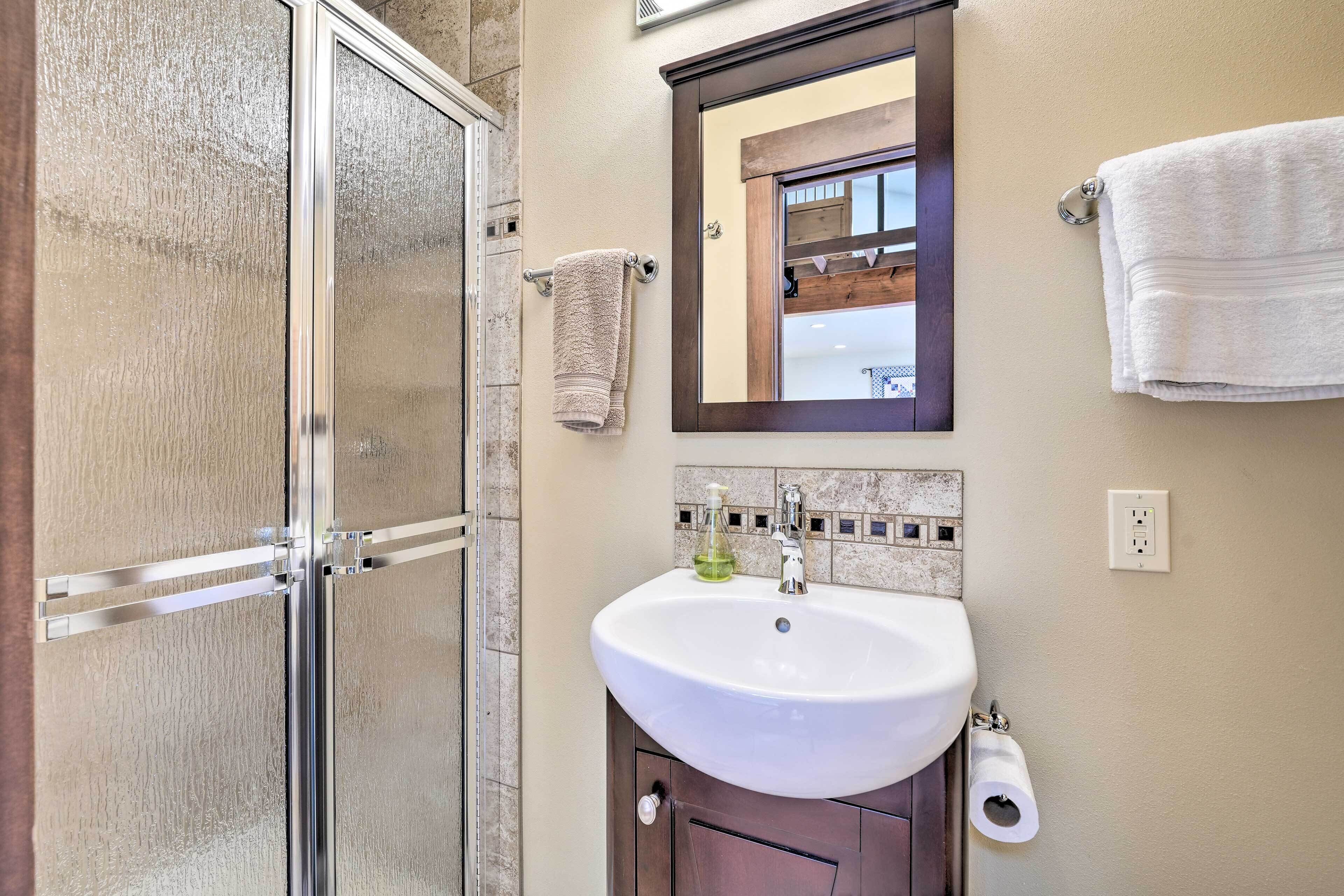 A bathroom with a glass shower door, a white sink with a mirror above it, and two towels hanging on the wall.
