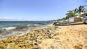 Una playa con costa rocosa, un bote y un edificio con balcón con vistas al mar.