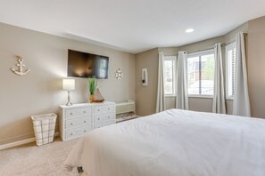 A bedroom with a large bed, a dresser, a TV mounted on the wall, and a window with curtains. - Walk to Shops & Lake: Pool-view Osage Beach Unit (Osage Beach)