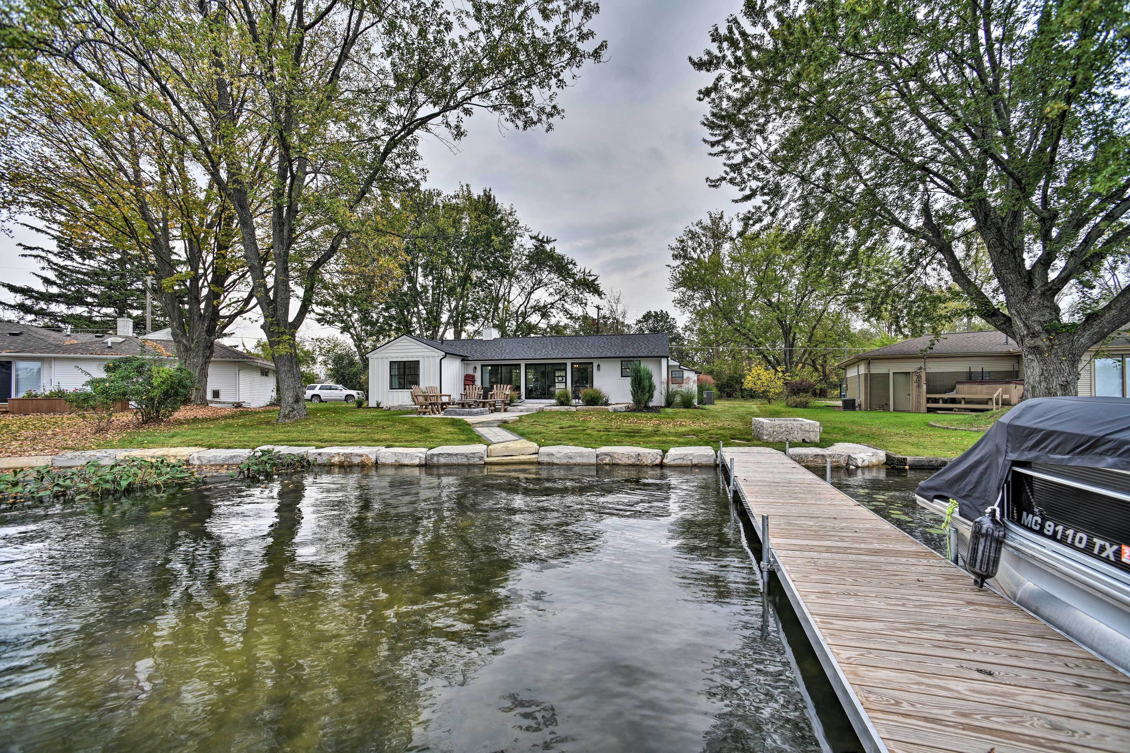 A residential area with a dock extending into a pond, surrounded by trees and houses.