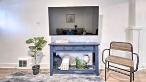 Un salon avec une console de couleur bleu foncé, une chaise en bois, une plante en pot, un globe terrestre et un téléviseur fixé au mur.