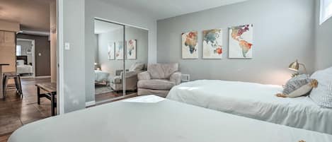 A bedroom with two beds, a sofa, and a mirror. There are three world maps on the wall.