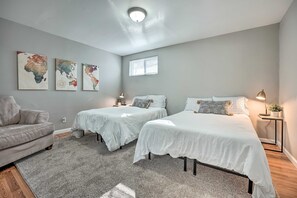 Un dormitorio con dos camas, un sofá gris, un cuadro con un mapa del mundo en la pared y una ventana con persianas.