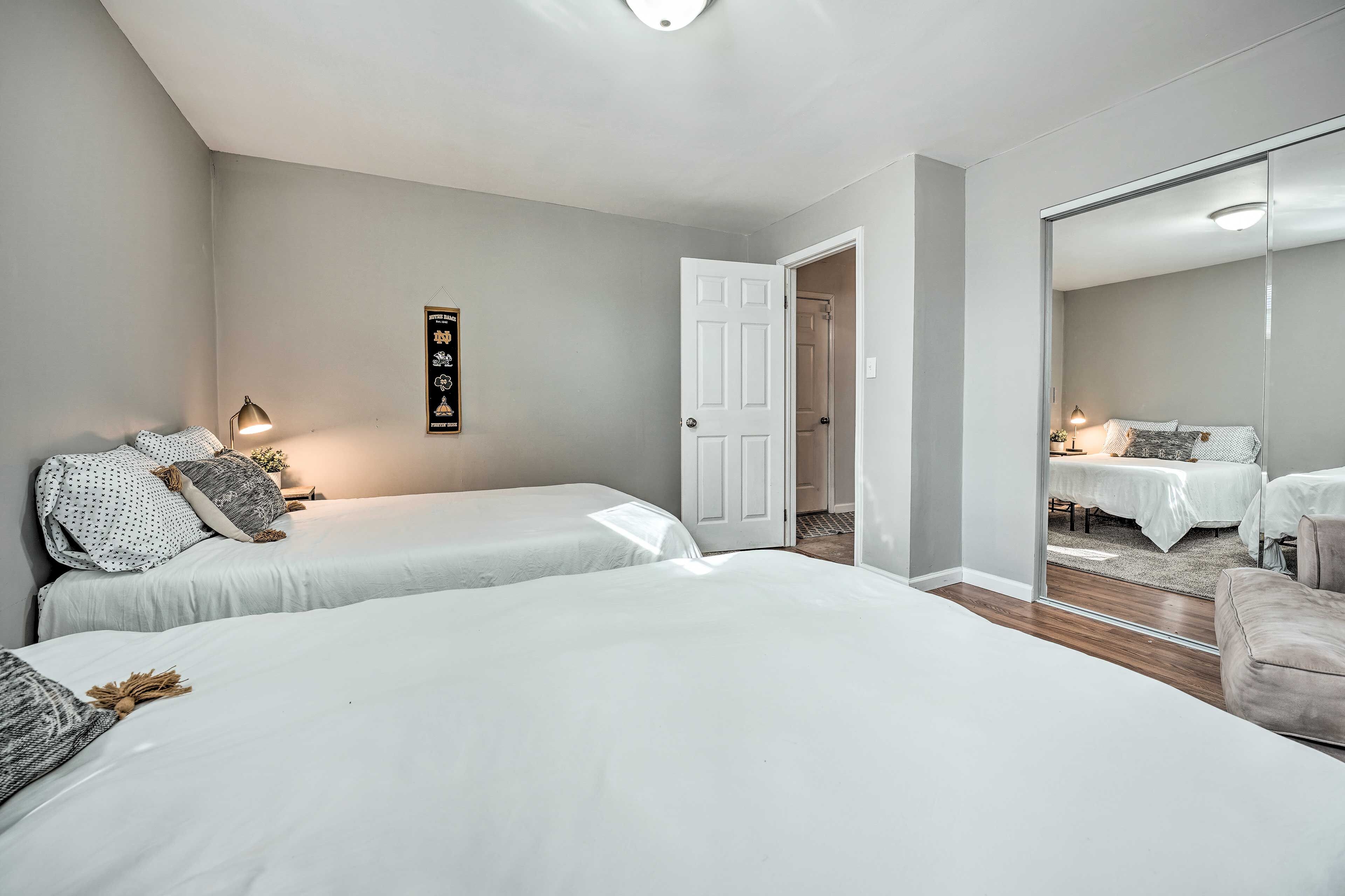 A bedroom with two beds, a large mirror, and a door leading to another room.