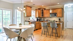 Una cocina moderna con armarios de madera, una isla central con taburetes de bar, una mesa de comedor con sillas y un amplio ventanal que proporciona luz natural.