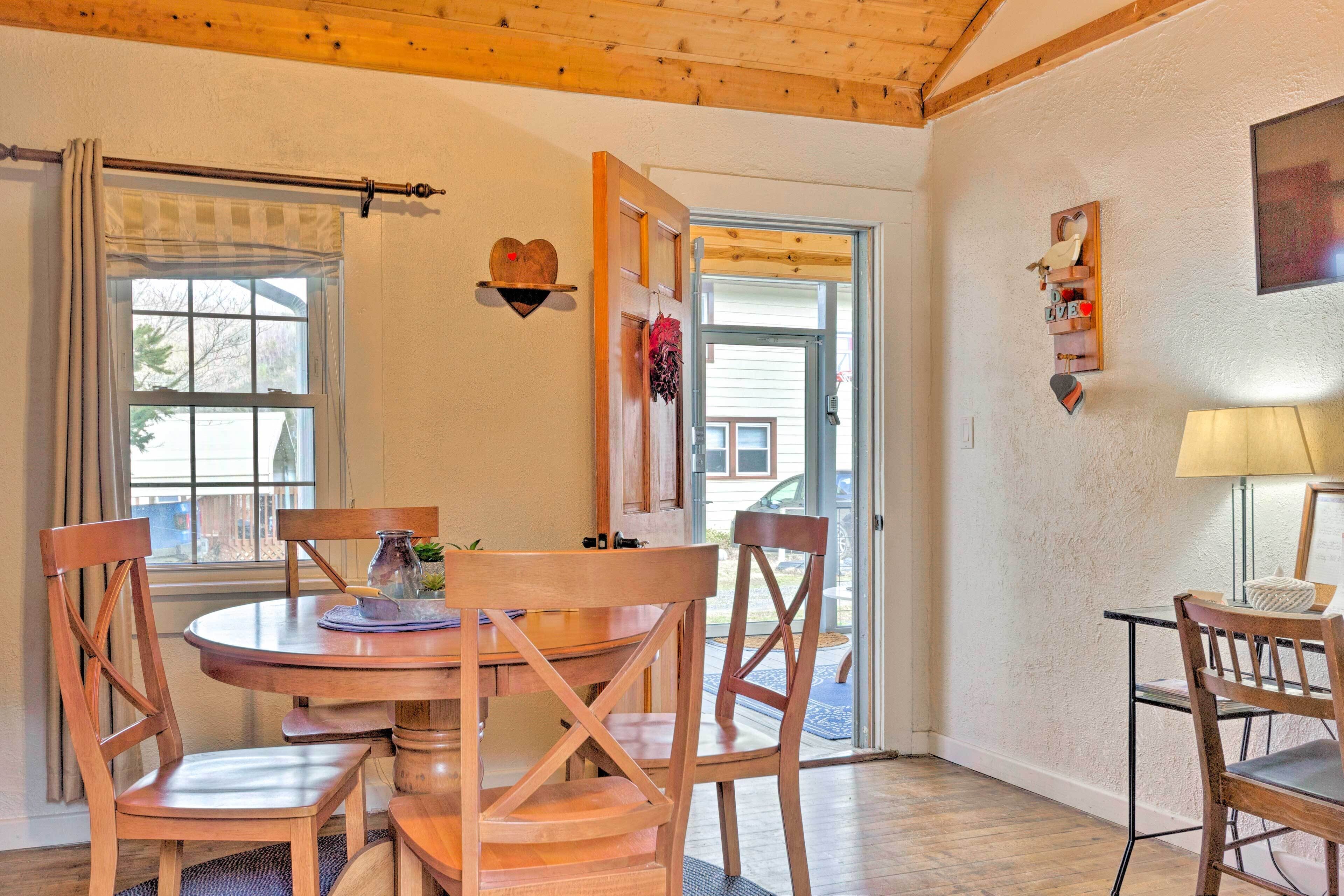 A dining area with a round wooden table, four wooden chairs, and a window with curtains.