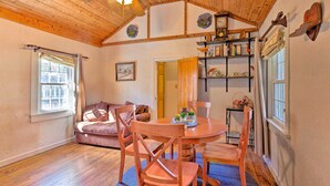 A cozy room with wooden floors, a round wooden table with chairs, a ceiling fan, and a bookshelf with various items. - Screened Porch: 'the Rock Cottage' in Hot Springs (Hot Springs)