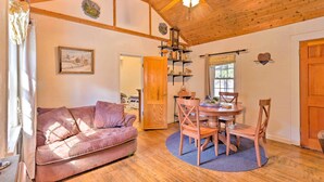 A cozy room with a wooden ceiling, a wooden dining table with chairs, a sofa, and a wooden door. - Screened Porch: 'the Rock Cottage' in Hot Springs (Hot Springs)
