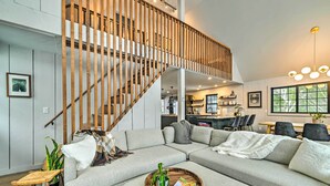 Un salon moderne avec un canapé d’angle, un escalier en bois et un coin repas à l’arrière-plan.
