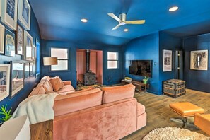 Ein Wohnzimmer mit blauer Wand, einem rosafarbenen Sofa, Holzboden, Deckenventilator und einem Fernseher.